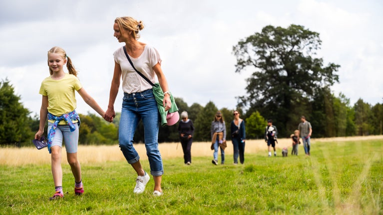 Families walking on grass exploring the park at Wimpole Estate, Cambridgeshire with trees in the background